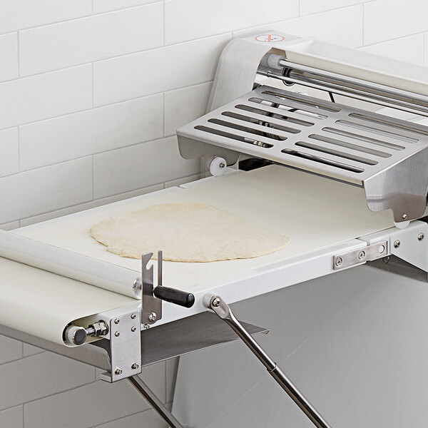 A white conveyor belt with a dough sheet on it.