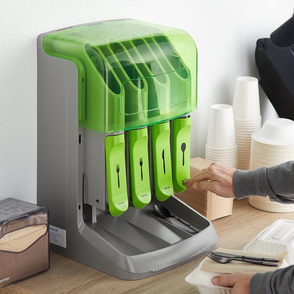 A person using a green Preserve Multi-Utensil Cutlery Dispenser on a counter in a corporate office cafeteria.