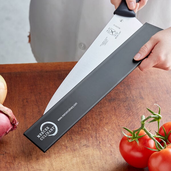 A person holding a Mercer Culinary knife with a polypropylene blade guard over tomatoes.