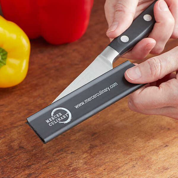 A person holding a Mercer Culinary knife with a red polypropylene blade guard.