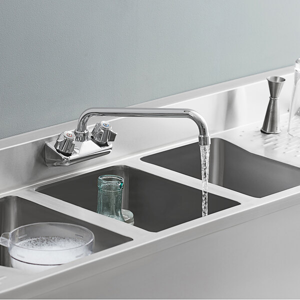 A stainless steel sink with a Regency wall mount faucet running water into a clear glass.