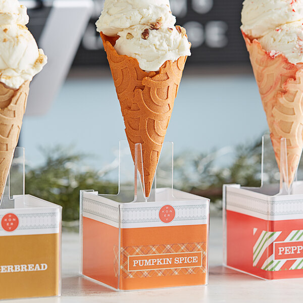 A Konery pumpkin spice waffle cone stand holding three ice cream cones with toppings.