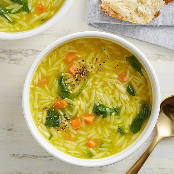 A bowl of orzo pasta in soup with vegetables.