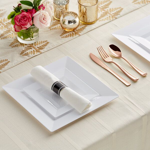 A white table set with Visions rose white plastic plates and classic rolled flatware.