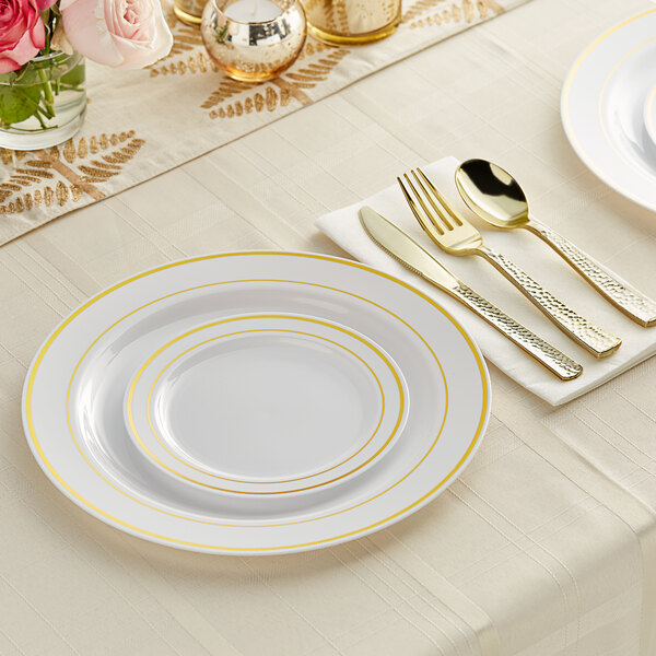 A table setting with white and gold Visions plastic plates and hammered flatware.