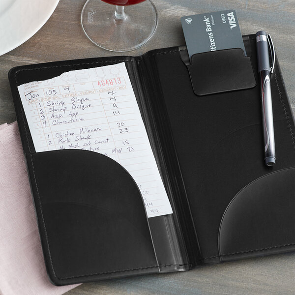 A black H. Risch double panel check presenter on a table with a pen and a note pad inside.