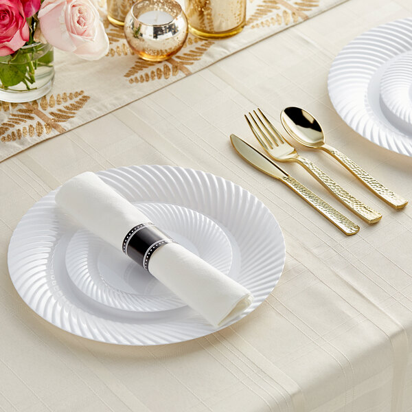 A white table setting with Visions white plastic plates, gold flatware, and silverware.