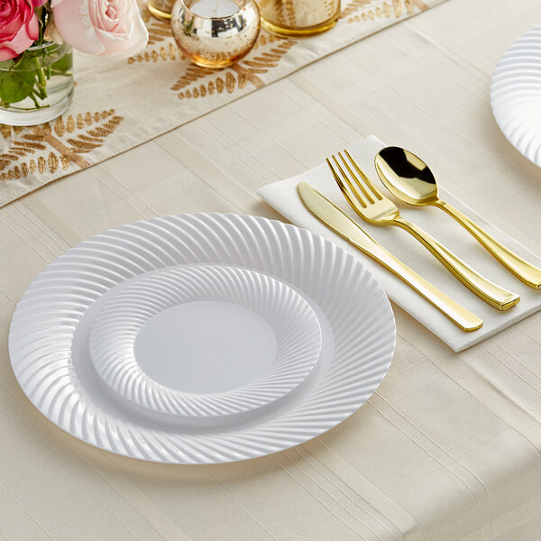 A white table setting with white wave plastic dinnerware and gold classic flatware on a white table.