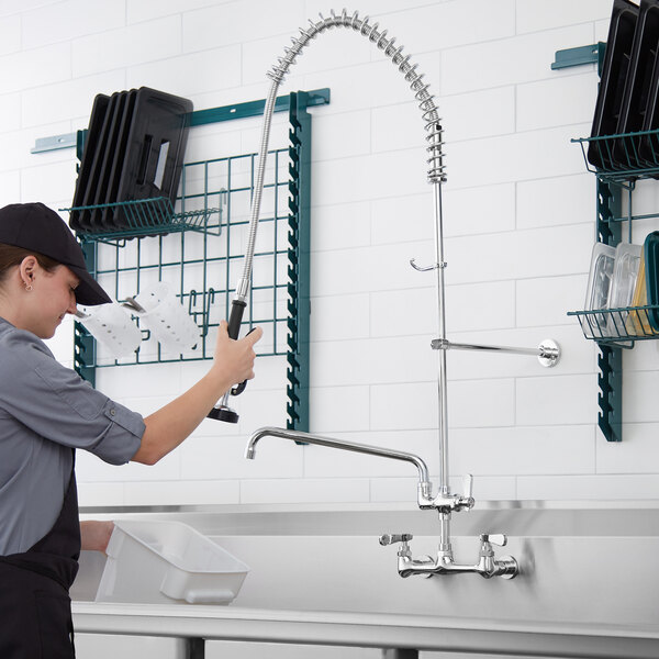 A woman in a black shirt using a black and silver Regency wall mount pre-rinse faucet over a sink.