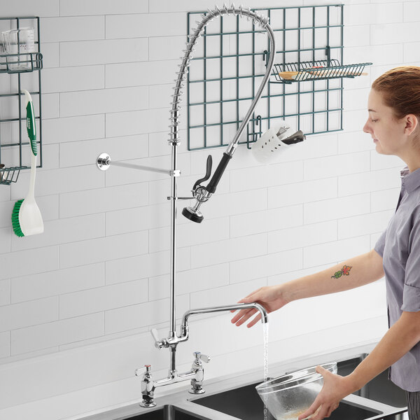 A woman using a Regency deck mount pre-rinse faucet to wash dishes in a sink.