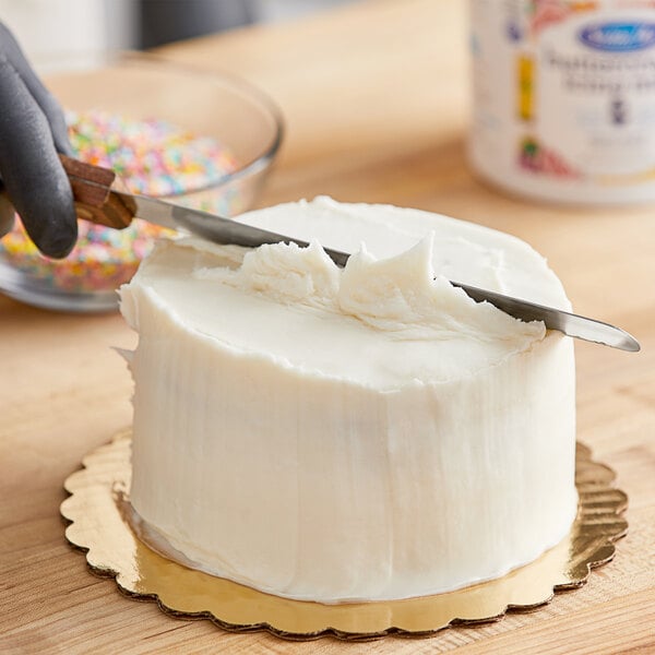 A person cutting a cake with Satin Ice White Vanilla Buttercream Icing