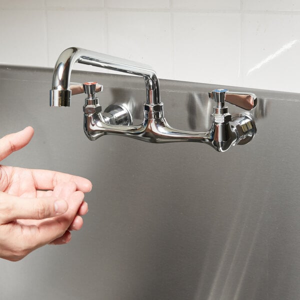 A hand reaching out to a 12" wall mounted swing spout swivel faucet.