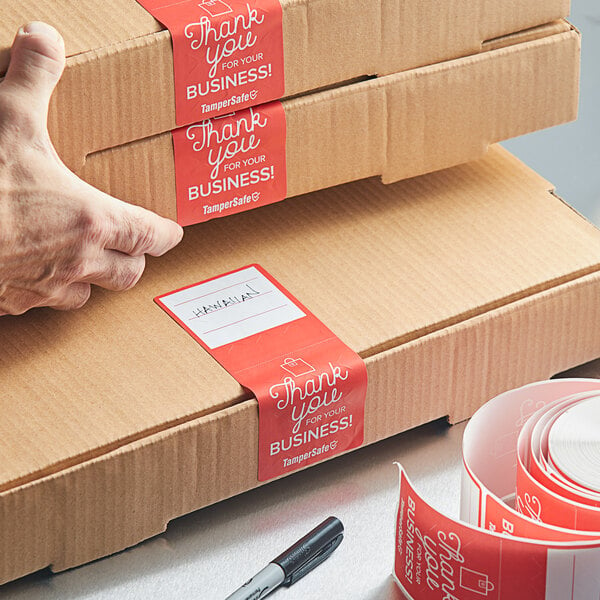 A hand holding a cardboard box with a stack of TamperSafe Thank You For Your Business red labels.