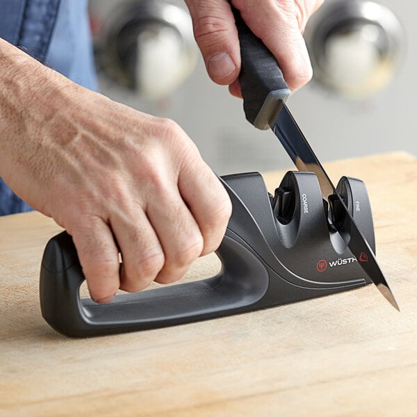A hand using a Wusthof 2-stage knife sharpener to sharpen a knife.