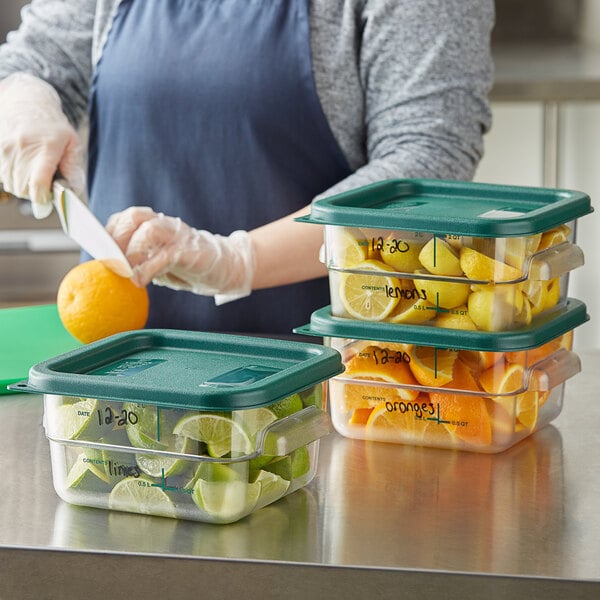 A person cutting an orange into a Vigor clear plastic food storage container with a green lid.