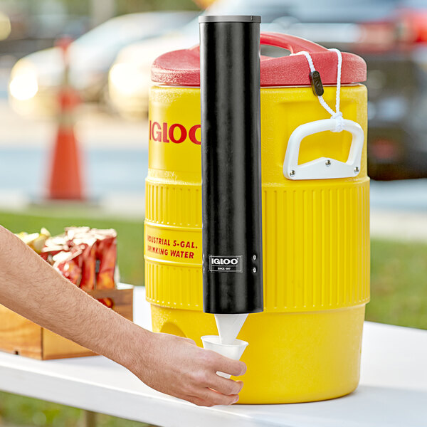 A hand pressing a black cylinder into a yellow cooler.