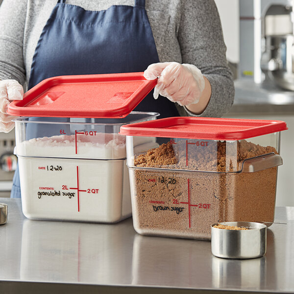 A woman holding a Vigor clear square polycarbonate food storage container with a red lid and food.