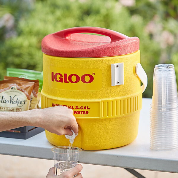 A person pouring water from an Igloo yellow insulated beverage dispenser.