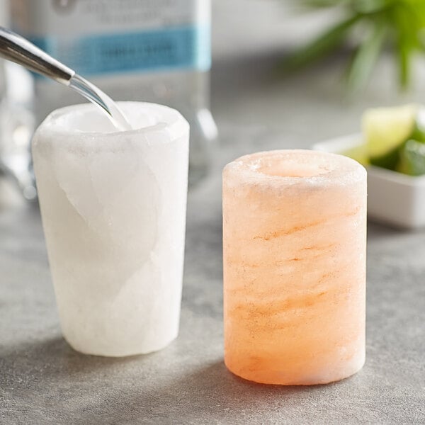 A Himalayan salt shot glass on a counter with a lime and a spoon.