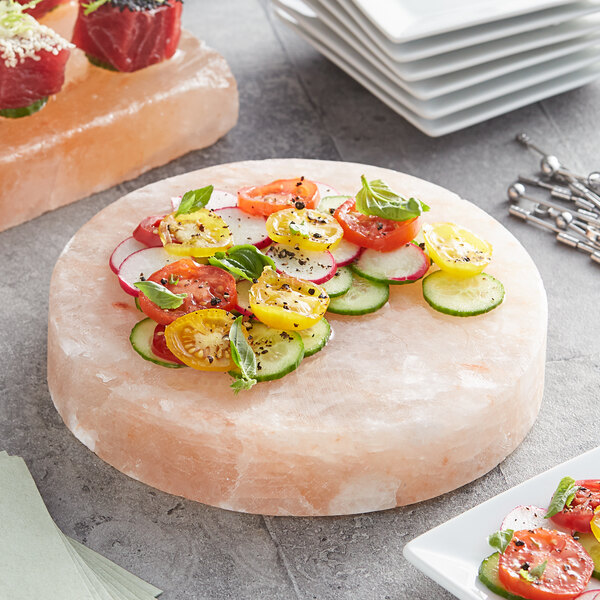 An 8" round Himalayan salt slab on a table with a plate of vegetables.