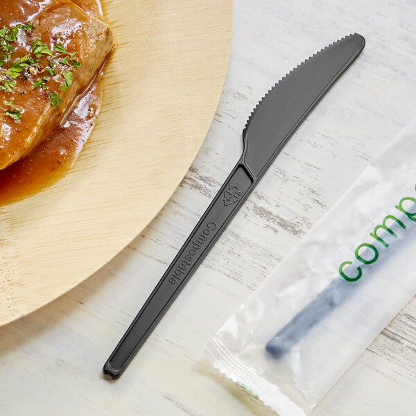 A EcoChoice black CPLA knife next to a plate with food.