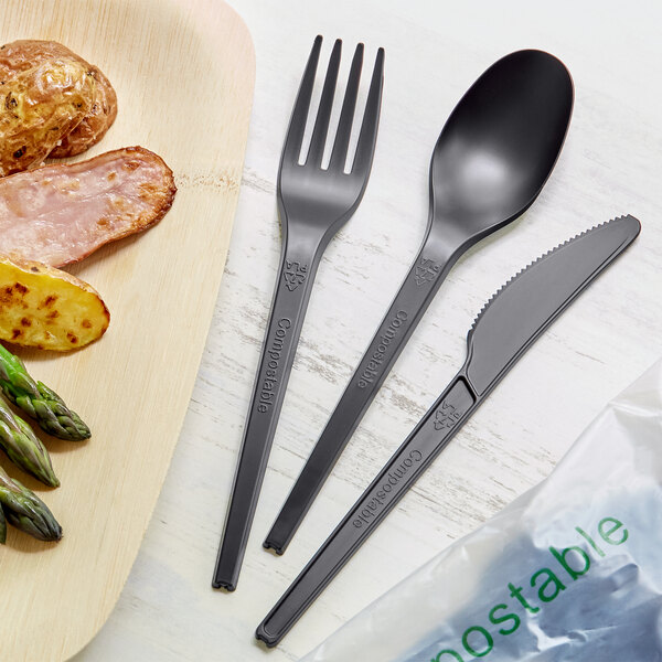 A plate of food with a black EcoChoice CPLA fork, knife, and spoon.
