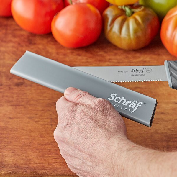 A hand holding a Schraf gray polypropylene knife blade guard over a tomato.