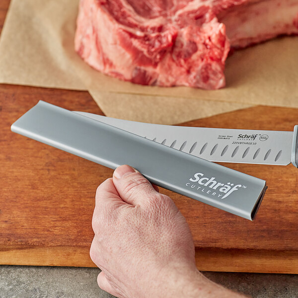 A hand holding a Schraf knife cutting meat on a counter.
