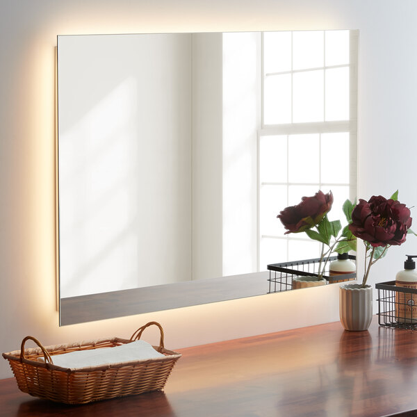 A Bobrick reversible LED backlit surface mounted mirror on a table in a white room.