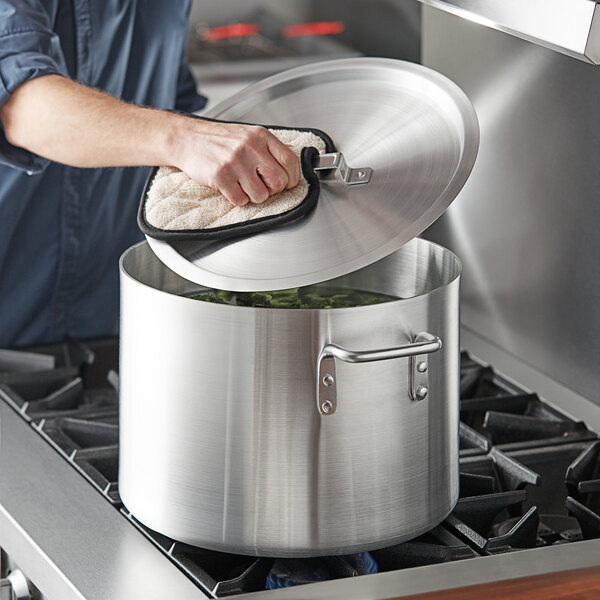 A person using a Choice aluminum sauce pot with a lid to cook green vegetables on a stove.