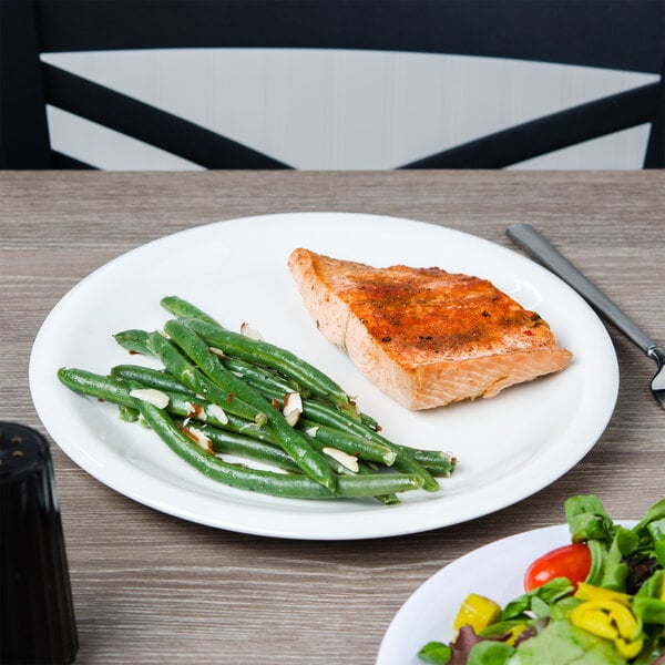A plate of food with cooked salmon and green beans on a Carlisle white melamine plate on a table.
