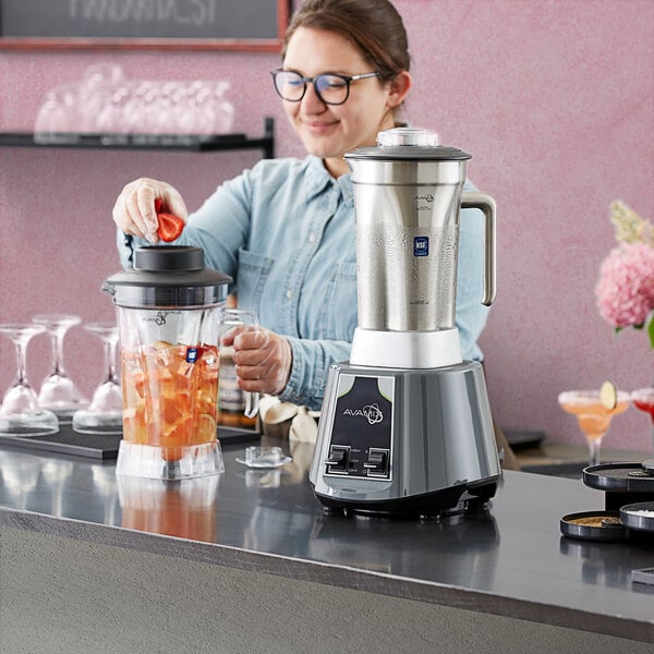 A woman using an AvaMix commercial blender to make a drink with ice cubes.