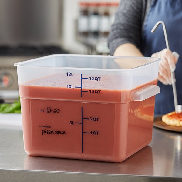 A woman preparing pizza in a Vigor translucent square food storage container on a counter.