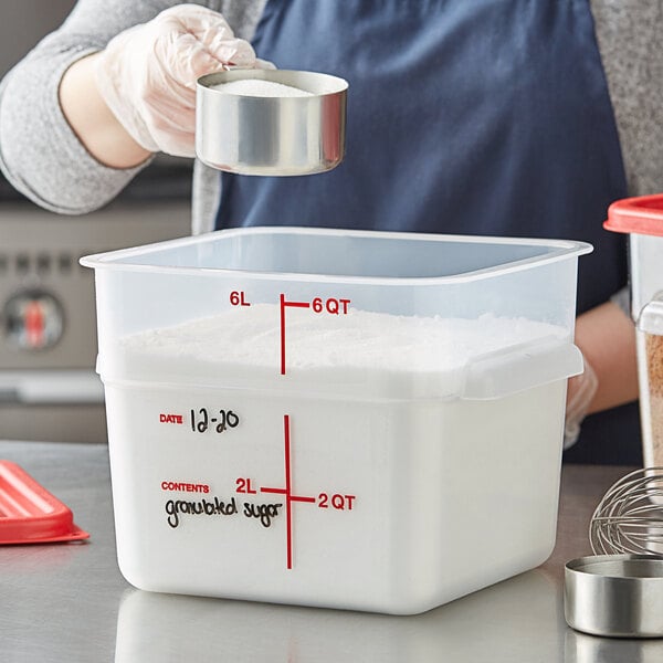 A woman pouring sugar from a silver pot into a white Vigor food storage container with red writing.