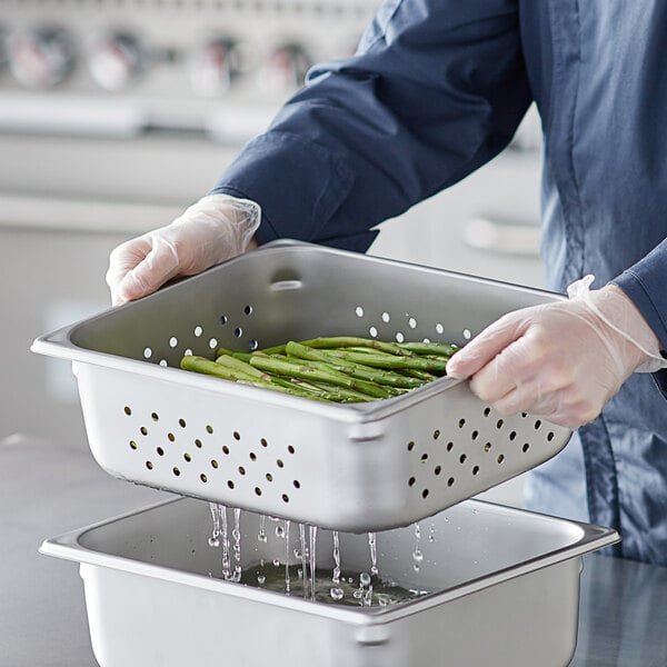 A person in a white coat holding a Vigor stainless steel pan filled with asparagus.