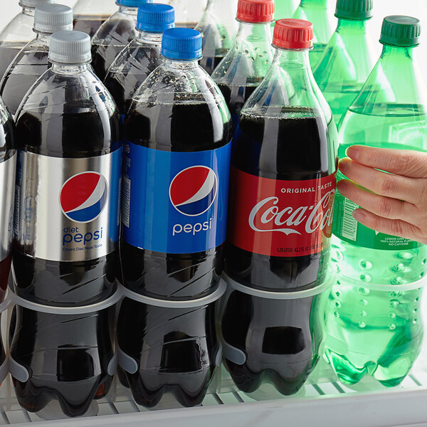 A hand holding a bottle of soda in a refrigerator.