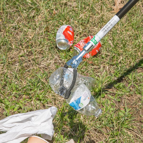 A person using an Unger NiftyNabber Pro to pick up a plastic bottle and soda cans from grass.