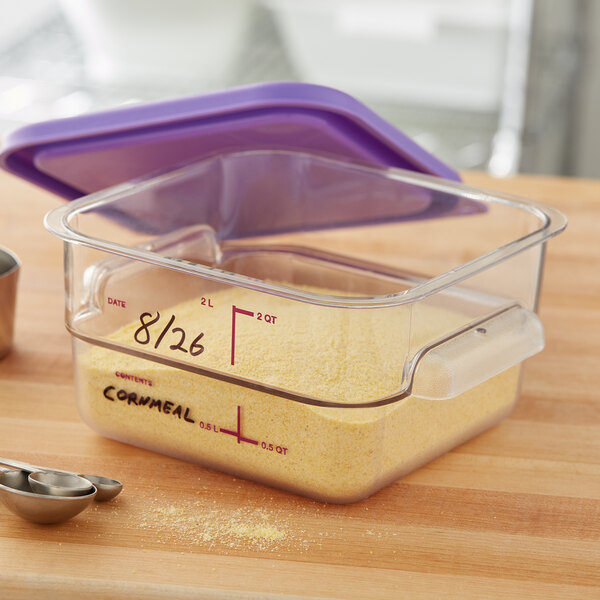 A Carlisle clear square polycarbonate food storage container on a kitchen counter with a plastic container of yellow cornmeal inside.
