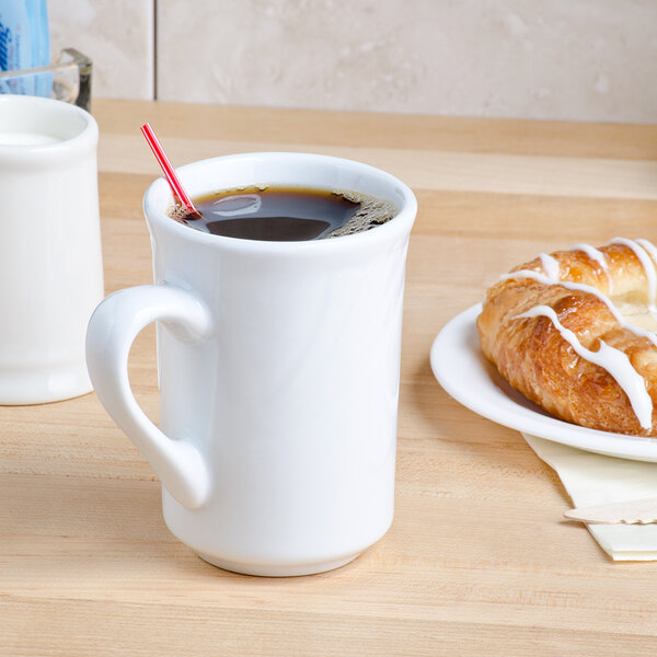 A Tuxton bright white china mug filled with coffee on a table with a pastry.
