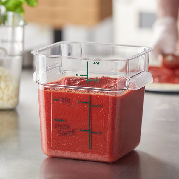 A Carlisle clear polycarbonate food storage container with red sauce in it on a counter.