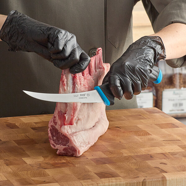 A person in black gloves using a Schraf curved boning knife to cut meat on a cutting board.