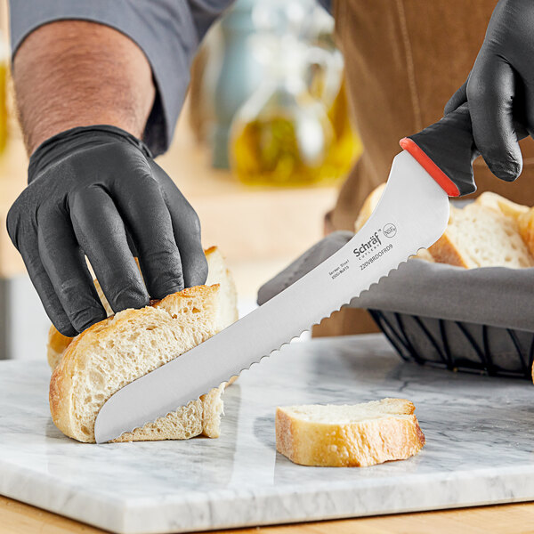 A hand in black gloves uses a Schraf serrated offset bread knife to cut bread.