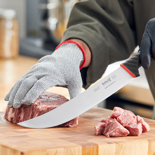 A person using a Schraf cimeter knife with a red handle to cut meat on a butcher shop counter.