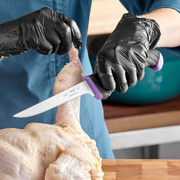A person in black gloves uses a Schraf purple narrow stiff boning knife to cut a chicken leg.