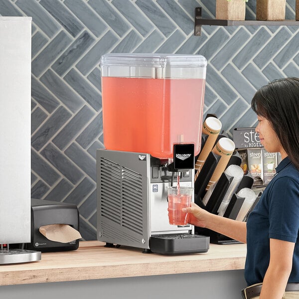 A woman pouring a drink into a Vollrath refrigerated beverage dispenser.