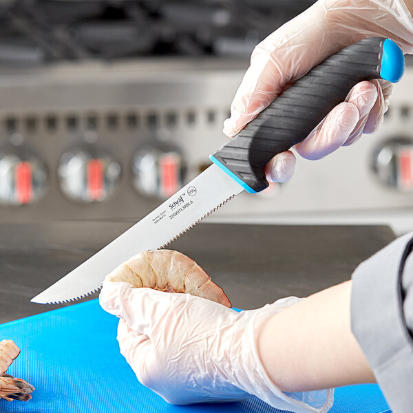 A gloved hand uses a Schraf serrated utility knife to cut shrimp on a counter.