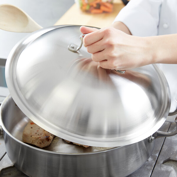 A chef using a Vollrath high domed lid to cover a large pan.