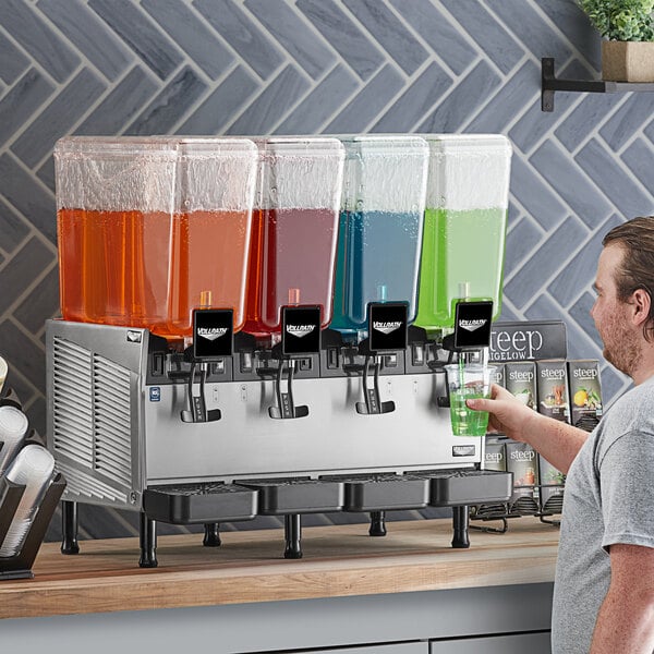 A man standing at a Vollrath refrigerated beverage dispenser filled with green liquid.