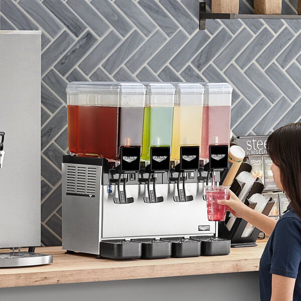 A woman using a Vollrath quadruple refrigerated beverage dispenser to pour a drink.