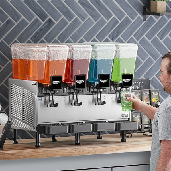A man pouring orange liquid into a Vollrath refrigerated beverage dispenser.